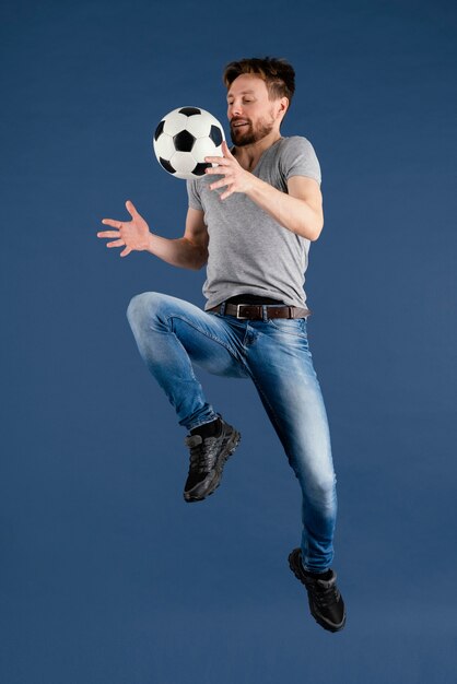 Jovem macho pulando com bola de futebol