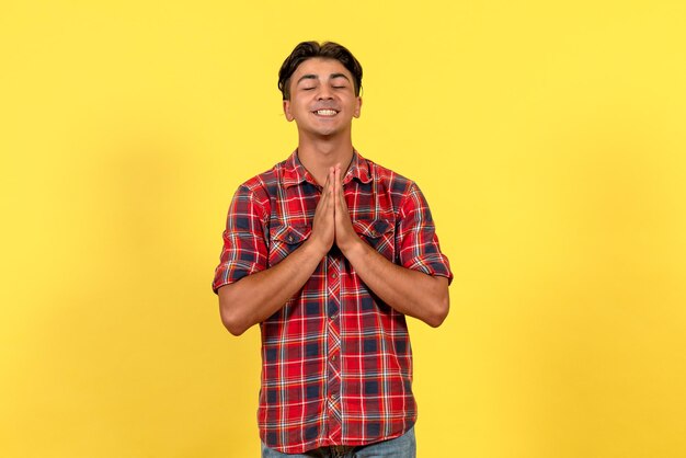 Jovem macho rezando sobre fundo amarelo de frente