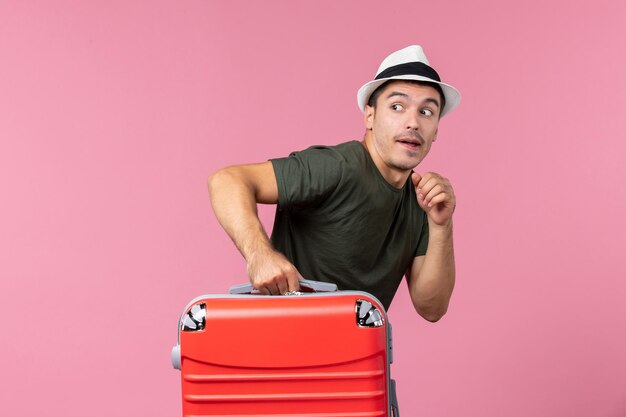 Jovem macho saindo de férias com bolsa vermelha no espaço rosa
