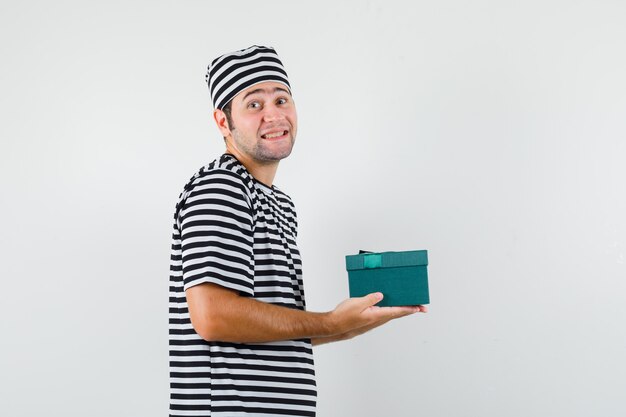 Jovem macho segurando a caixa de presente em t-shirt, chapéu e olhando feliz.