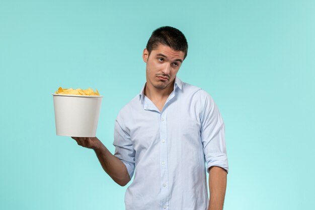Jovem macho segurando a cesta com batata frita na superfície azul claro de frente