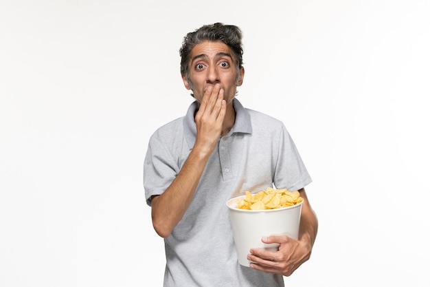 Jovem macho segurando a cesta com batata frita na superfície branca de frente