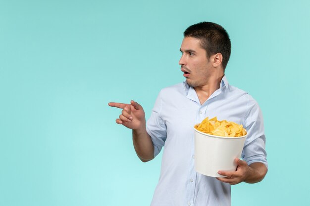 Jovem macho segurando a cesta com batatas fritas e assistindo filme na mesa azul