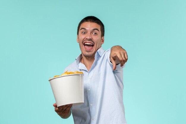 Jovem macho segurando a cesta com batatas fritas e assistindo filme na superfície azul