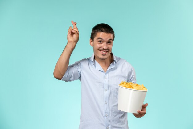 Jovem macho segurando a cesta com batatas fritas e sorrindo na superfície azul