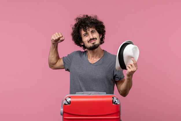 Jovem macho segurando o chapéu e se preparando para as férias no espaço rosa