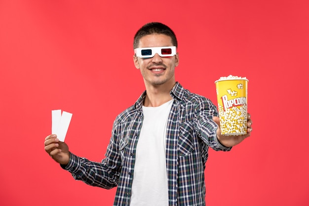 Foto grátis jovem macho segurando pipoca e bilhete em óculos de sol de frente no filme de cinema de parede vermelha