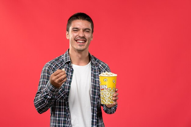 Jovem macho segurando pipoca e rindo em um filme de cinema com parede vermelha clara