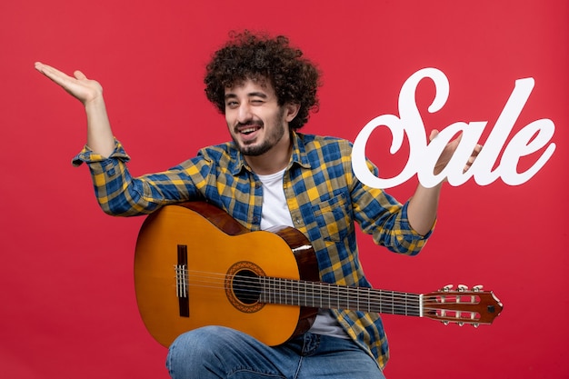 Foto grátis jovem macho sentado com guitarra na parede vermelha concerto de música ao vivo venda de cor