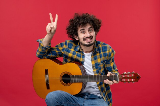 Jovem macho sentado com guitarra na parede vermelha tocar música músico cor aplausos concerto ao vivo