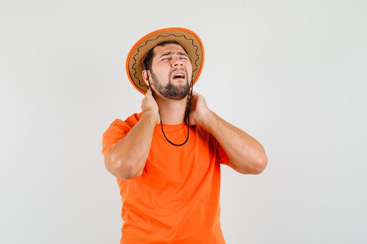 Foto grátis jovem macho sofrendo de dor no pescoço em t-shirt laranja, chapéu e parecendo cansado, vista frontal.