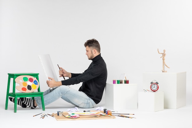 Jovem macho tentando desenhar pintura com borla na parede branca artista pintura arte cor pintura desenho