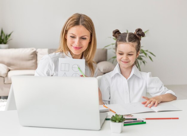 Foto grátis jovem mãe ajudando a filha em uma aula on-line