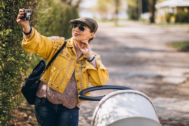 Jovem mãe andando com carrinho de bebê no parque e usando o telefone