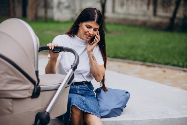 Jovem mãe caminhando no parque com um carrinho de bebê e falando ao telefone