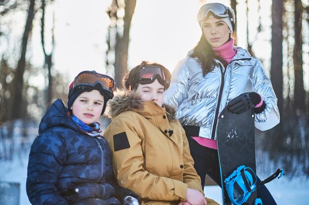 Jovem mãe com dois filhos está posando para o fotógrafo na floresta ensolarada de inverno.