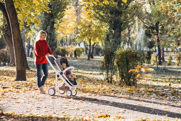 Jovem mãe com filha bebê andando no parque no outono