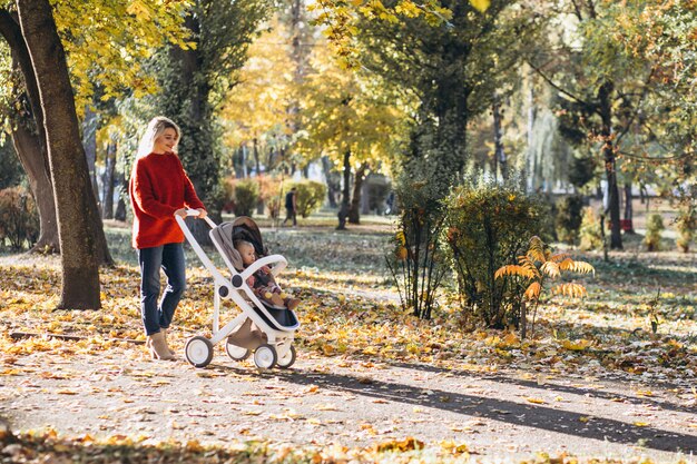 Jovem mãe com filha bebê andando no parque no outono