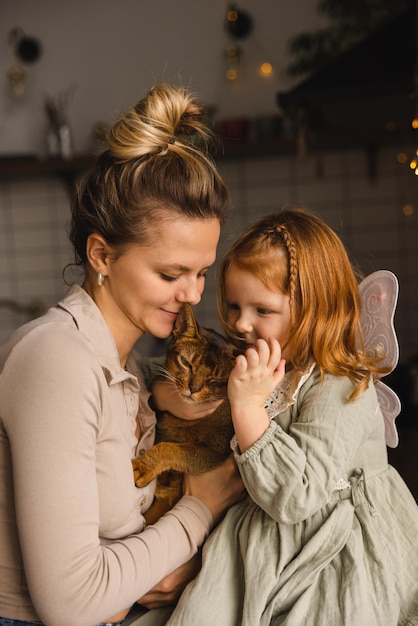 Jovem mãe de pele clara com filhinha ruiva está brincando com seu gato em casa conceito de família