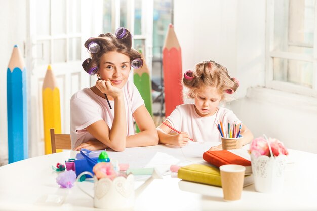 jovem mãe e a filha pequena desenhando a lápis em casa