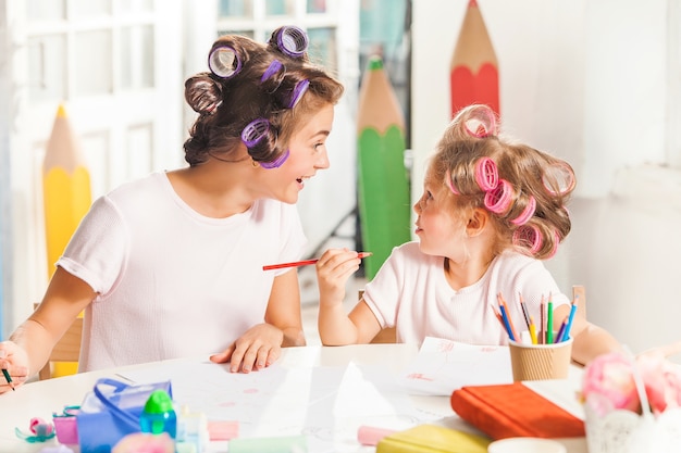 jovem mãe e a filha pequena desenhando a lápis em casa