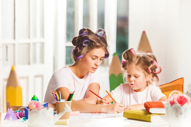 jovem mãe e a filha pequena desenhando a lápis em casa