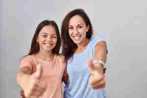 Foto grátis jovem mãe e filha em pé sobre fundo branco aprovando fazendo gesto positivo com mão polegares para cima sorrindo e feliz pelo gesto de vencedor de sucesso