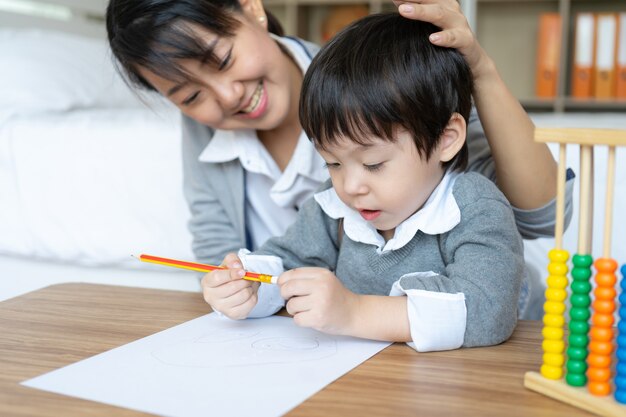 Jovem mãe ensinando seu filho escrever no papel com amor