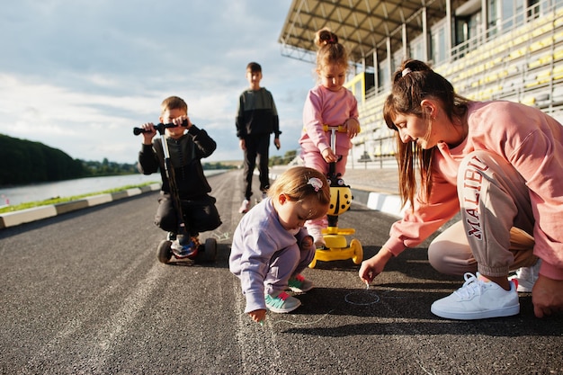 Jovem mãe estilosa com quatro filhos Família esportiva ao ar livre passa tempo livre ao ar livre com patinetes e patins