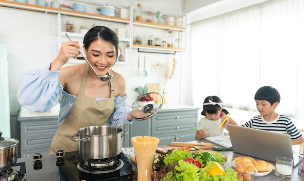 Jovem mãe solteira asiática fazendo comida enquanto cuida da criança na cozinha