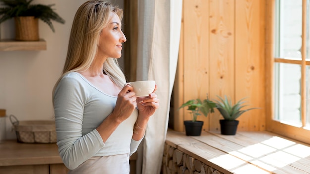 Foto grátis jovem mãe tomando uma xícara de café enquanto olha pela janela