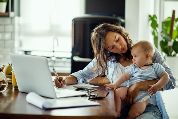 Jovem mãe trabalhadora planejando o orçamento doméstico enquanto está com seu bebê em casa