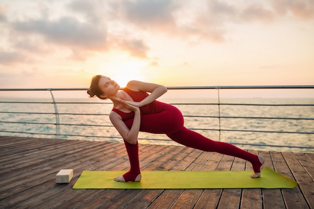 Foto grátis jovem magro mulher atraente bonita fazendo yoga de manhã no nascer do sol pelo mar, estilo de vida saudável