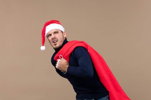 Jovem masculino carregando uma sacola de presentes no chão marrom natal feriado papai noel