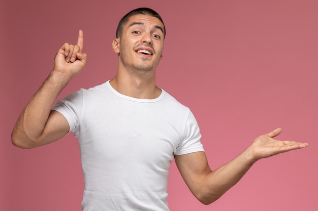 Jovem masculino com camiseta branca, posando com o dedo levantado em um fundo rosa