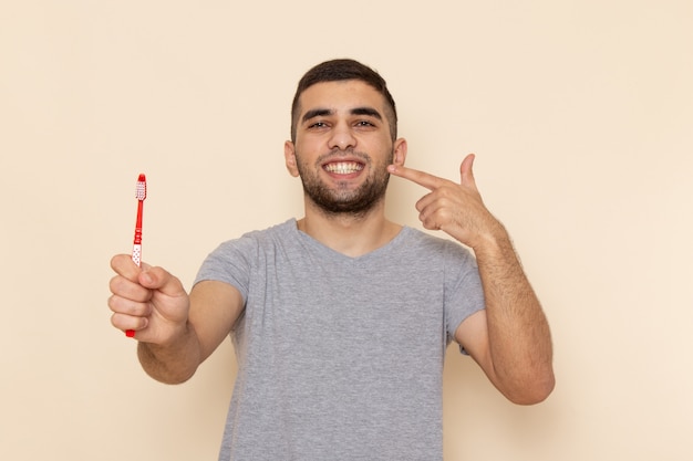 Jovem masculino com camiseta cinza limpando os dentes em bege