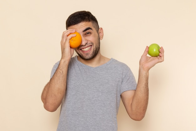 Jovem masculino com camiseta cinza segurando uma maçã e uma mesa laranja