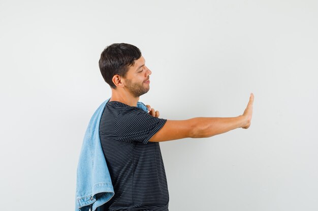 Foto grátis jovem masculino com camiseta segurando o paletó nas costas e mostrando gesto de recusa