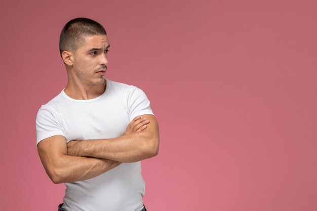 Jovem masculino de camisa branca posando com as mãos cruzadas no fundo rosa