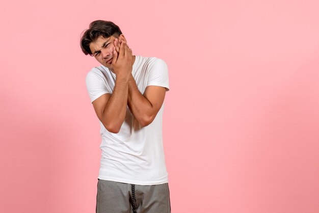 Jovem masculino de camiseta branca com dor de dente no fundo rosa.
