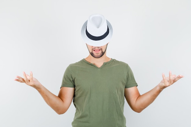 Jovem masculino levantando as mãos com uma camiseta e um chapéu verdes e parecendo engraçado