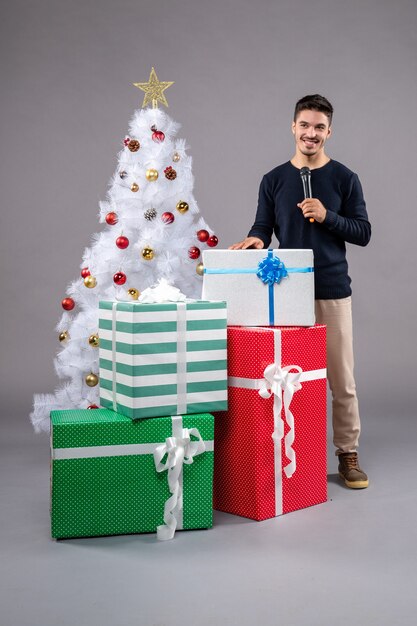 Jovem masculino segurando o microfone de frente com presentes no piso cinza. presente de natal de ano novo