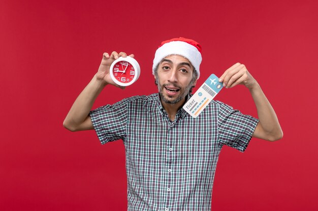 Jovem masculino segurando o tíquete e o relógio em um fundo vermelho.