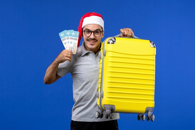 Jovem masculino segurando passagens e uma bolsa pesada no avião de férias com fundo azul