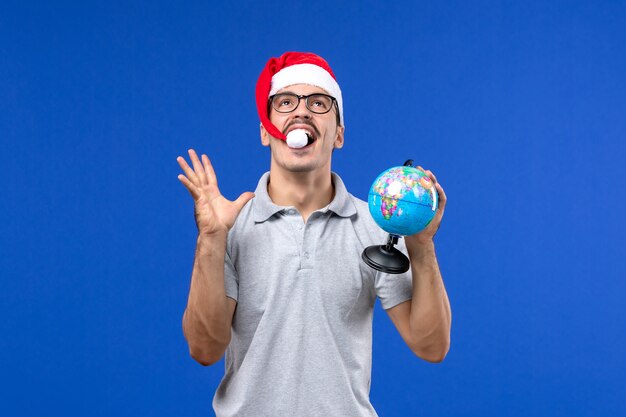 Jovem masculino segurando um globo terrestre na parede azul, avião, viagem de férias masculino