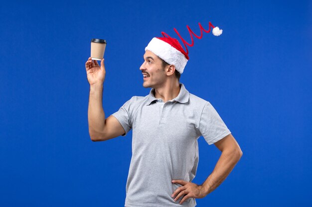 Jovem masculino segurando uma xícara de café de plástico na parede azul, feriado masculino de ano novo