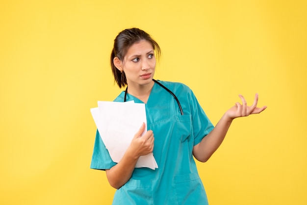 Jovem médica com camisa médica e papéis sobre fundo amarelo, vista frontal