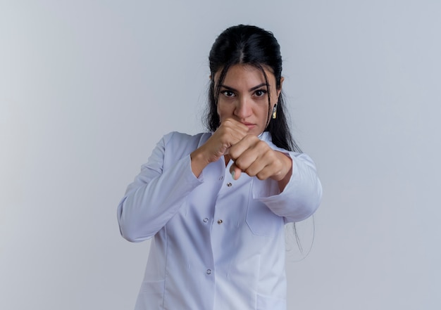 Foto grátis jovem médica confiante vestindo túnica médica e olhando fazendo gesto de boxe isolado