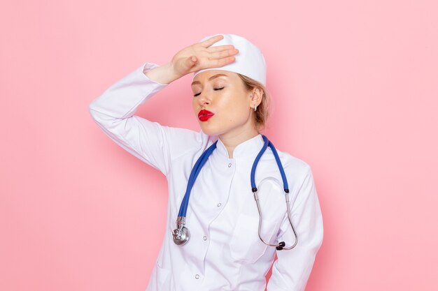 Jovem médica de terno branco com estetoscópio azul, vista frontal, posando no espaço rosa