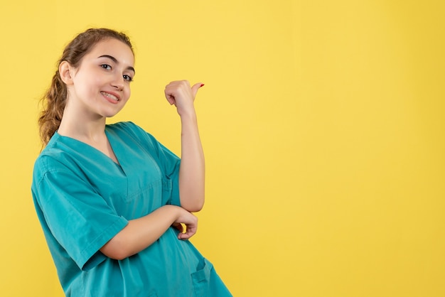 Jovem médica em terno médico, vista frontal, sorrindo sobre fundo amarelo